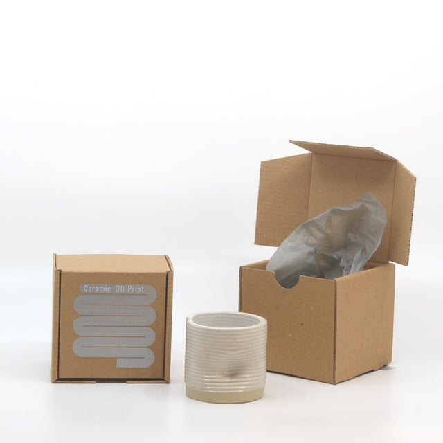 ceașca ceramică imprimată 3D cu cutia în care este ambalată. cutia din carton craft cu autocolant argintiu pe care scrie ceramic 3D print